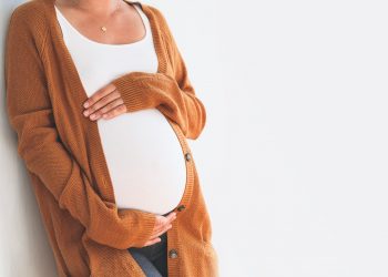 Beautiful pregnant woman touching her belly with hands on a white background.